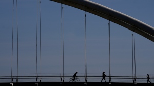 People enjoy the above seasonal warm weather as they cross the Humber River on a bridge in Toronto on Monday, March 4, 2024. THE CANADIAN PRESS/Nathan Denette