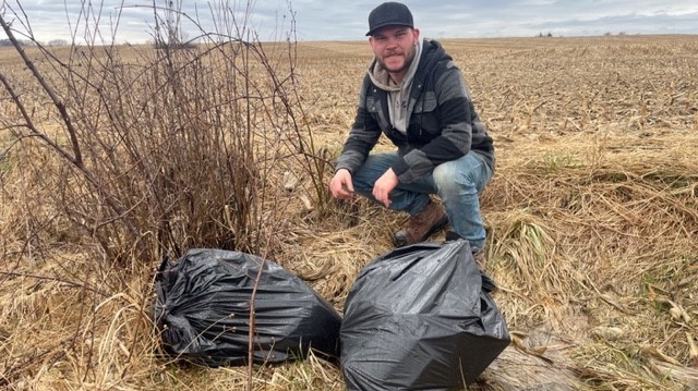 Mark Rimmelzwaan crouches behind two bags of trash illegally dumped on the fringe of his farm on Tuesday, March 26, 2024. (Sean Irvine/CTV News London) 