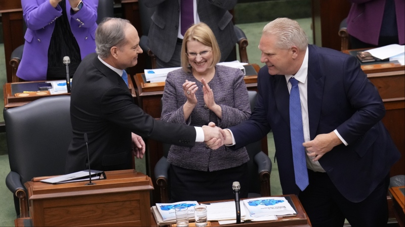 Finance Minister Peter Bethlenfalvy shakes hands with Premier Doing Ford as Health Minister Sylvia Jones looks on after Bethlenfalvy tabled the Ontario provincial budget at the legislature at Queen's Park in Toronto on Tuesday, March 26, 2024. (The Canadian Press/Nathan Denette)
