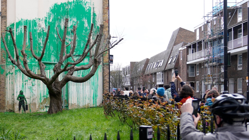 People look at a new Banksy painting on a wall in London, Monday, March 18, 2024. (AP Photo/Alastair Grant) 
