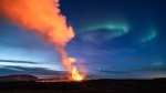 A view of the lava flowing from the volcano backdropped by the Northern Lights, near the town of Grindavik, Iceland, early Monday, March 25, 2024. (AP Photo/Marco di Marco)