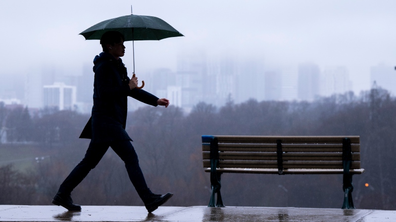 The Toronto skyline sits shrouded in fog as a man walks in the rain on Thursday December 28, 2023.(Frank Gunn/The Canadian Press)