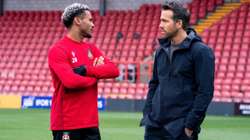 This image released by FX shows Dior Angus, left, and Ryan Reynolds in a scene from the docuseries 'Welcome to Wrexham,' which follows owners Reynolds and Rob McElhenney as they takeover the lower-league Welsh soccer team Wrexham AFC. (Patrick McElhenney / FX via AP)