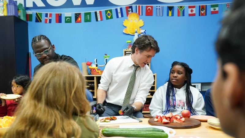 Prime Minister Justin Trudeau talks to ten year old Chakai as cuts fruit next to chef Jason Simpson at photo opportunity as they prepare food for a lunch program at the Boys and Girls Club East Scarborough, in Toronto, before an announcement to launch a National School Food Program, Monday, April 1, 2024. THE CANADIAN PRESS/Chris Young