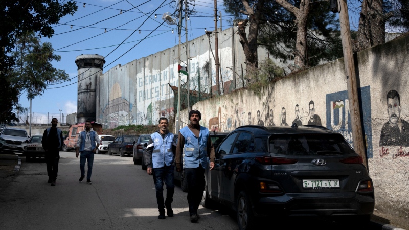 Staff of the United Nations Relief and Works Agency for Palestinian Refugees in the Near East (UNRWA) walk along Israel's separation barrier to their office at Aida Refugee Camp in the West Bank city of Bethlehem, Feb. 20, 2024. (AP Photo/Maya Alleruzzo)