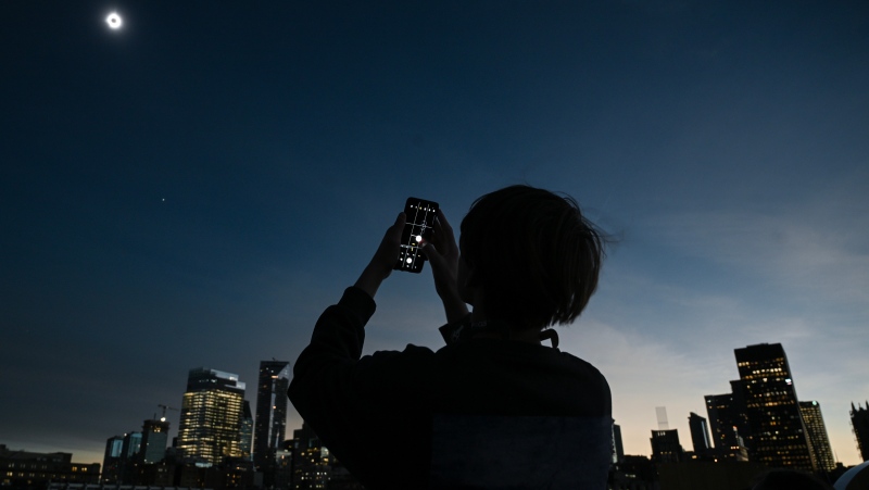 A person takes a photograph of the sun during totality as the moon passes between it and the earth resulting in a total solar eclipse, in Montreal, Monday, April 8, 2024. (Graham Hughes / The Canadian Press)