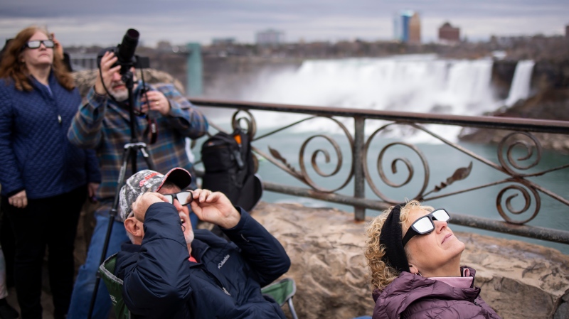 Visitors use special glasses to watch the total solar eclipse from Niagara Falls, Ont., on Monday, April 8, 2024. (THE CANADIAN PRESS/Aaron Lynett)