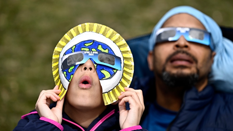 Dezaray Butts and her father Douglas observe the solar eclipse in Kingston, Ont., on Monday, April 8, 2024. (Justin Tang / The Canadian Press) 