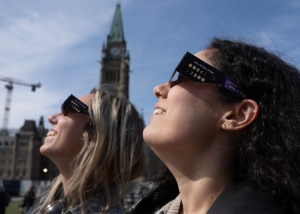 Two women wear protective glasses as they take in the solar eclipse from Parliament Hill, Monday, April 8, 2024 in Ottawa. (Adrian Wyld/THE CANADIAN PRESS)