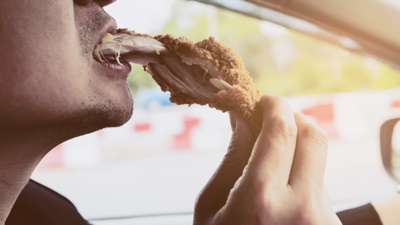 A man eats fried chicken inside a car in this image from Shutterstock.com 