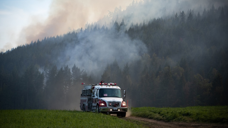 Firefighters drive across a farm while monitoring a controlled burn near a wildfire northwest of Vernon, B.C., Wednesday, Aug. 25, 2021. THE CANADIAN PRESS/Darryl Dyck