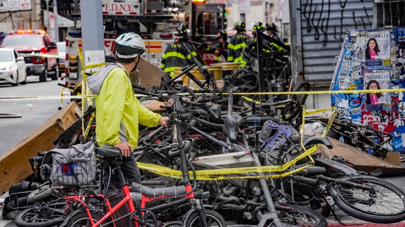 A biker stops to look at a pile of e-bikes in the aftermath of a fire in Chinatown, which authorities say started at an e-bike shop and spread to upper-floor apartments, Tuesday June 20, 2023, in New York. (Source: AP Photo/Bebeto Matthews, File)