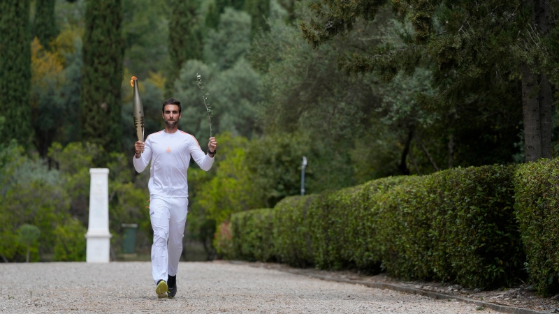 The first torch bearer, Greek olympic gold medalist Stefanos Douskos, returns from the monument to Pierre de Coubertin, in the background, after the official ceremony of the flame lighting for the Paris Olympics, at the Ancient Olympia site, Greece, Tuesday, April 16, 2024. (AP Photo/Thanassis Stavrakis)