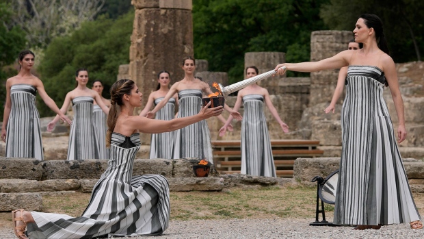 Actress Mary Mina, playing high priestess, right, lights a torch during the official ceremony of the flame lighting for the Paris Olympics, at the Ancient Olympia site, Greece, Tuesday, April 16, 2024. (AP Photo/Thanassis Stavrakis)