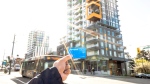 A person holds up a Compass Card in front of PCI Developments' Yarrow East Village building on East Hastings Street. (TranLink)