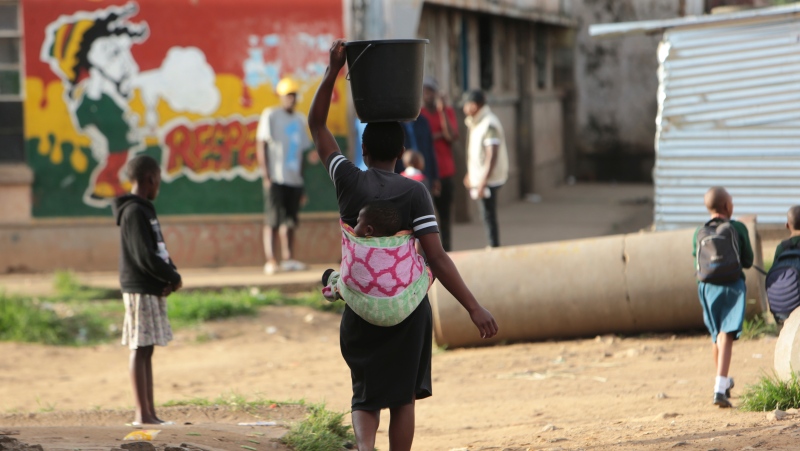 A woman carries her baby and a bucket of water in Harare on April 6, 2020. (AP Photo/Tsvangirayi Mukwazhi)