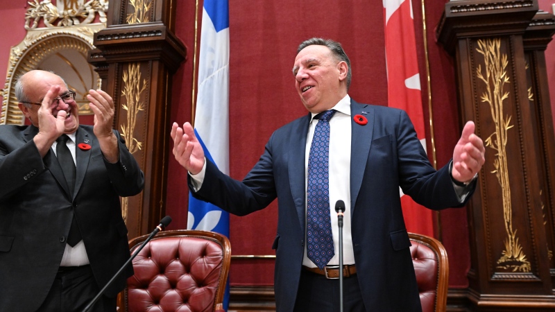 Quebec Premier François Legault waves as he arrives at the beginning of a government caucus meeting as MNA Mario Laframboise applauds, Wednesday, November 9, 2022. (THE CANADIAN PRESS/Jacques Boissinot)