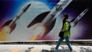 A woman walks past a banner showing missiles being launched, in northern Tehran, Iran, Friday, April 19, 2024. (AP Photo/Vahid Salemi)