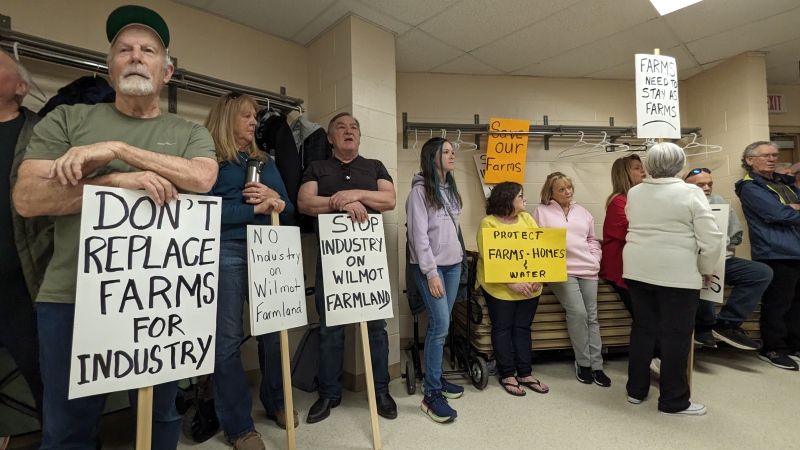 People hold signs inside a town hall meeting hosted by the NDP opposing the acquisition of farmland in Wilmot Township for an unidentified industrial project. (Dan Lauckner/CTV Kitchener)