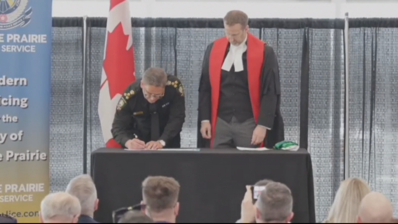 Dwayne Lakusta, left, signs a document as Justice Chris Millsap looks on at a swearing-in ceremony on April 19, 2024, for Lakusta as the City of Grande Prairie's police chief. (CTV News Edmonton)