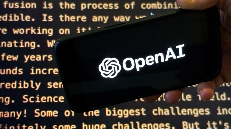 File - The OpenAI logo appears on a mobile phone in front of a screen showing part of the company website in this photo taken on Nov. 21, 2023 in New York. (AP Photo/Peter Morgan, File)