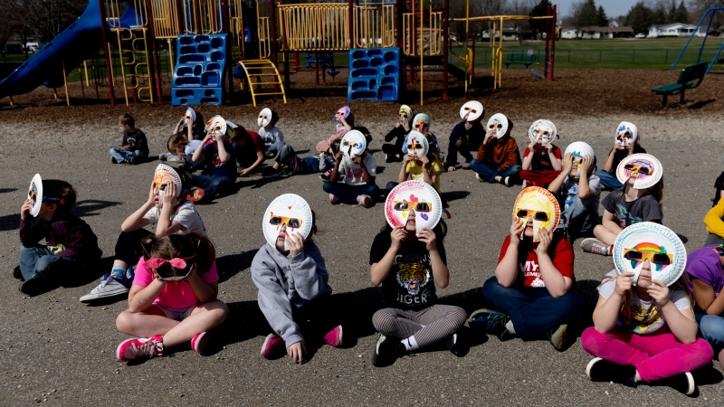 Students from two kindergarten classes, escorted outside by their teachers Amy Johnston and Wendy Sheridan, stare toward the sky with their specially-made glasses to watch the solar eclipse on Monday, April 8, 2024, at Myers Elementary School in Grand Blanc, Mich. The paper plates, which help provide further safety for their eyes, were added on and decorated by each student in their classrooms as a project leading up to the big day. (Jake May,The Flint Journal)