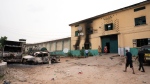 People walk past burned vehicles in front of a correctional facility in Owerri, Nigeria, on Monday, April 5, 2021. (David Dosunmu / AP Photo)