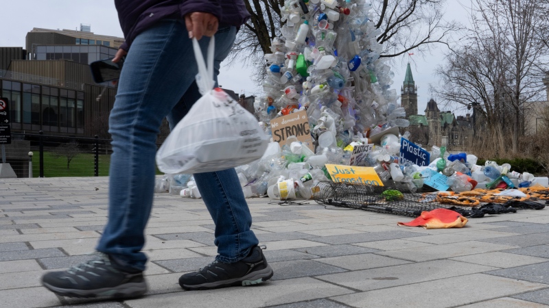 A person carries food in a plastic bag past a plastic public art installation outside the a United Nations conference on plastics on Tuesday, April 23, 2024 in Ottawa. THE CANADIAN PRESS/Adrian Wyld