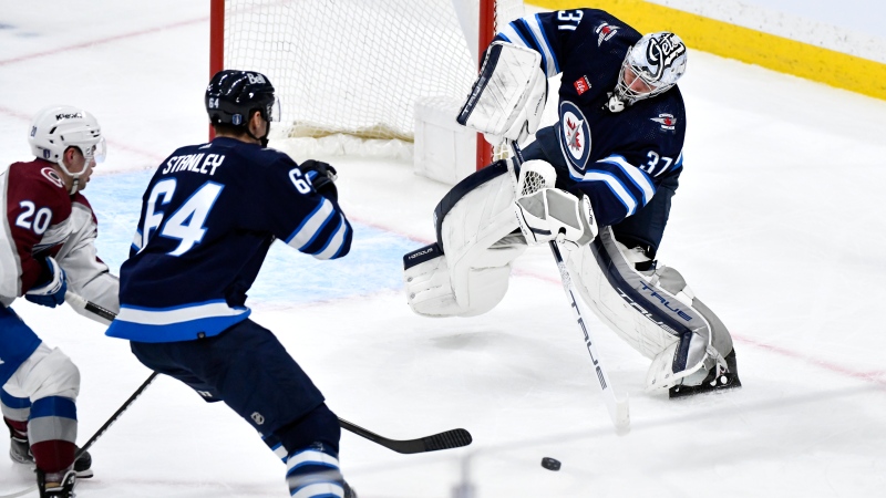 Winnipeg Jets goaltender Connor Hellebuyck (37) clears the puck as Logan Stanley (64) defends against Colorado Avalanche's Ross Colton (20) during the first period in Game 2 of their NHL hockey Stanley Cup first-round playoff series in Winnipeg, Tuesday April 23, 2024. (Fred Greenslade/The Canadian Press) 