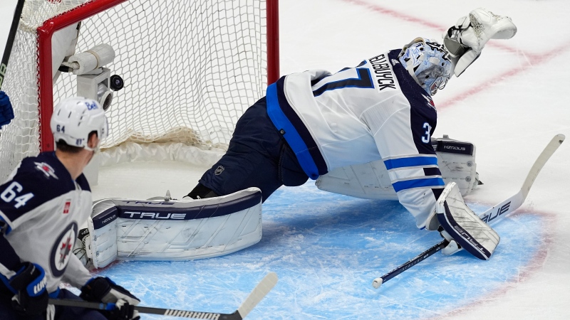 Winnipeg Jets goaltender Connor Hellebuyck, right, allows in a goal on a shot by Colorado Avalanche left wing Artturi Lehkonen (not shown) as Jets defenseman Logan Stanley (64) looks on in the first period of Game 4 of an NHL Stanley Cup first-round playoff series Sunday, April 28, 2024, in Denver. (AP Photo/David Zalubowski)