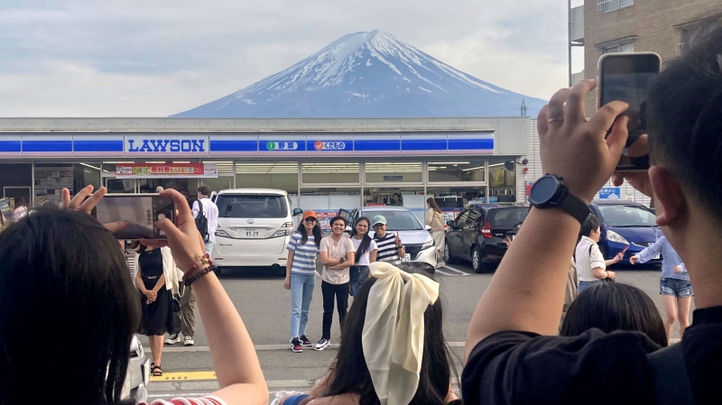 Visitors take a photo in front of a convenience store at Fujikawaguchiko, Japan, with a backdrop of Mount Fuji on April 28, 2024. (Kyodo News via AP)
