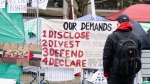 A man reads a sign of demands posted outside a pro-Palestinian encampment set up on McGill University's campus in Montreal, Tuesday, April 30, 2024. THE CANADIAN PRESS/Christinne Muschi