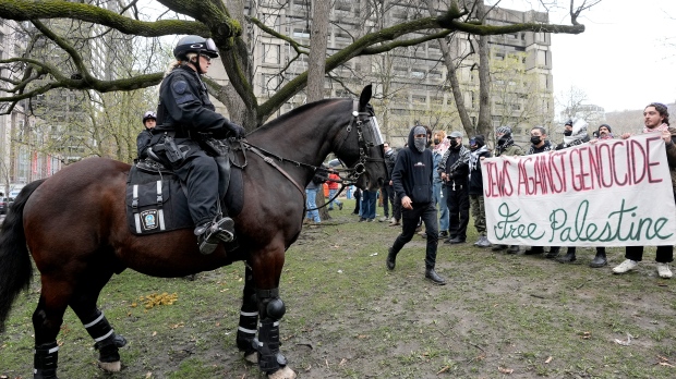 Jewish Pro-Palestinian activists hold a banner as mounted police officers look on at the outskirts of a protest encampment on the grounds of McGill University, in Montreal, Thursday, May 2, 2024. (Ryan Remiorz, The Canadian Press)