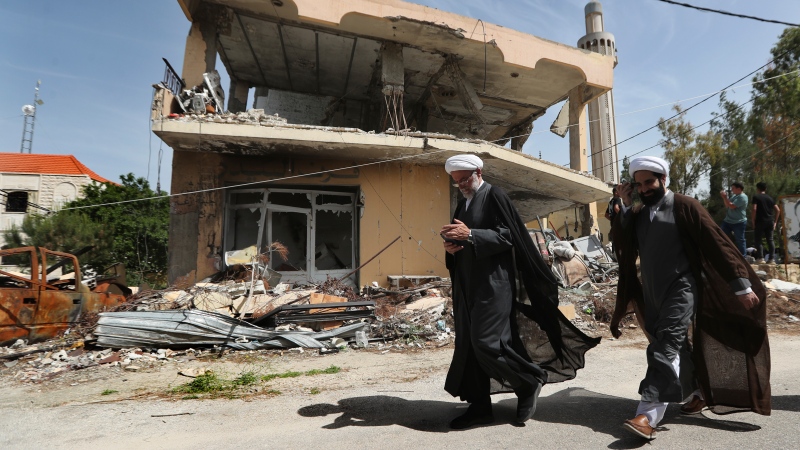 Shiite clerics pass in front of a house that was destroyed by an Israeli airstrike, in Hanine village, south Lebanon, Thursday, April 25, 2024. (AP Photo/Mohammed Zaatari) 