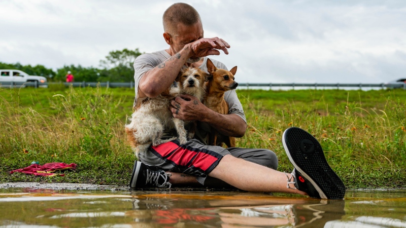 Tim McCanon sits on the road with his dogs after being rescued by the Community Fire Department during severe flooding on Friday, May 3, 2024, in New Caney, Texas. (Raquel Natalicchio / Houston Chronicle via AP)