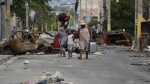Residents walk past a burnt car blocking the street as they evacuate the Delmas 22 neighbourhood to escape gang violence in Port-au-Prince, Haiti, Thursday, May 2, 2024. AP / Ramon Espinosa