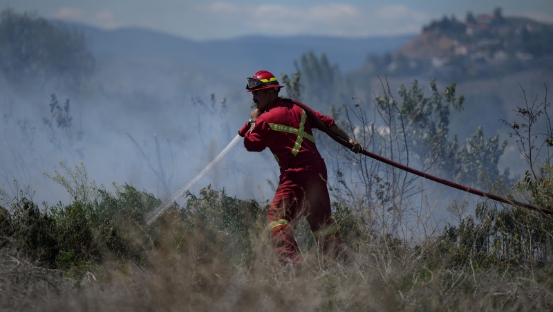 A firefighter directs water on a grass fire burning on an acreage behind a residential property in Kamloops, B.C., Monday, June 5, 2023. (THE CANADIAN PRESS/Darryl Dyck)