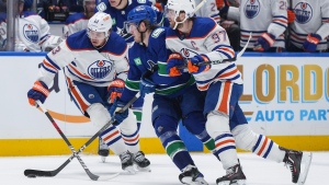 Edmonton Oilers' Connor McDavid, right, checks Vancouver Canucks' Brock Boeser as Edmonton's Mattias Janmark, back left, watches during the first period in Game 1 of an NHL hockey Stanley Cup second-round playoff series, in Vancouver, on Wednesday, May 8, 2024. THE CANADIAN PRESS/Darryl Dyck