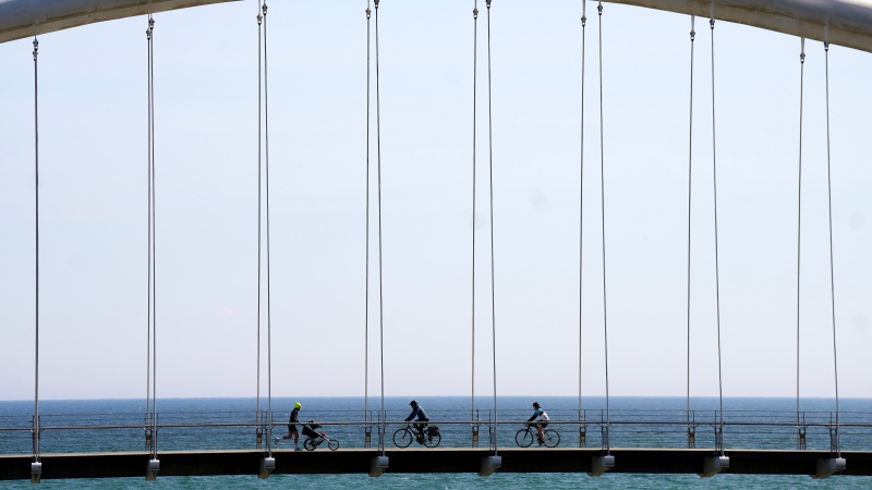 People enjoy the above seasonal warm weather as they cross the Humber River on a bridge in Toronto on Monday, March 4, 2024. THE CANADIAN PRESS/Nathan Denette