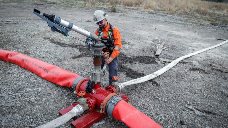 Justin Massie, wildfire specialist with Fire & Flood Emergency Service Ltd., adjusts a valve on a wildfire suppression water cannon along highway 881 near Gregoire Lake Estates southeast of Fort McMurray, Wednesday, May 15, 2024. (Jeff McIntosh / The Canadian Press) 