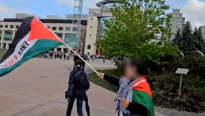 Hayfa Abdelkhaleq waving Palestinian flag as someone walks up behind her and pulls off her hijab. (Katelyn Wilson/CTV News).