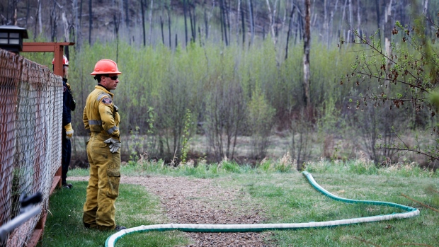 A firefighters monitors a wildfire sprinkler hose on May 16, 2024, in the evacuated neighbourhood of Grayling Terrace in Fort McMurray, Alta. (Jeff McIntosh/The Canadian Press)