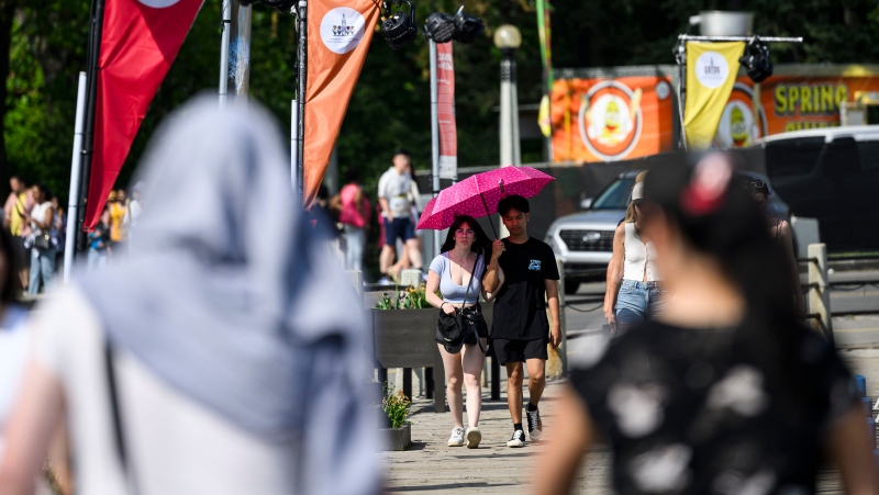 People use an umbrella to shield themselves from the sun as they walk near Dow's Lake in Ottawa, on Victoria Day, Monday, May 20, 2024. THE CANADIAN PRESS/Justin Tang
