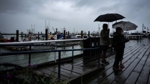 People are silhouetted as they use umbrellas to shield themselves from the rain on the boardwalk overlooking the Steveston Fisherman's Wharf, in Richmond, B.C., on Monday, July 24, 2023. (Darryl Dyck/The Canadian Press)