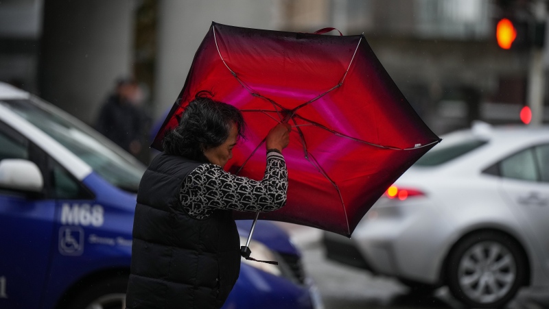 A woman struggles with an umbrella in the wind as rain falls in Vancouver, on Monday, September 25, 2023. THE CANADIAN PRESS/Darryl Dyck