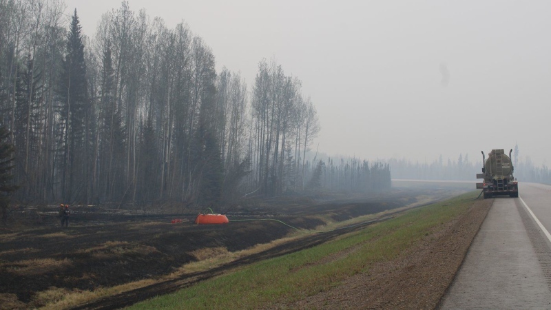 Firefighters working the Parker Lake wildfire, designated G90267 by the B.C. Wildfire Service, are seen in a staging area along Highway 97 looking south with a water bladder and fire hose set up among charred grassland in a May 15, 2024, handout photo. THE CANADIAN PRESS/HO-BC Wildfire Service