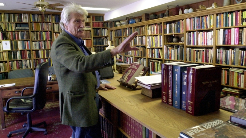Schuyler Jones talks about the bookcases he built that line his library Monday, Feb. 6, 2006, in Wichita, Kan. Jones, a globe-trotting American adventurer whose exploits drew comparisons to iconic movie character Indiana Jones, has died. He was 94. (Dave Williams/The Wichita Eagle via AP)