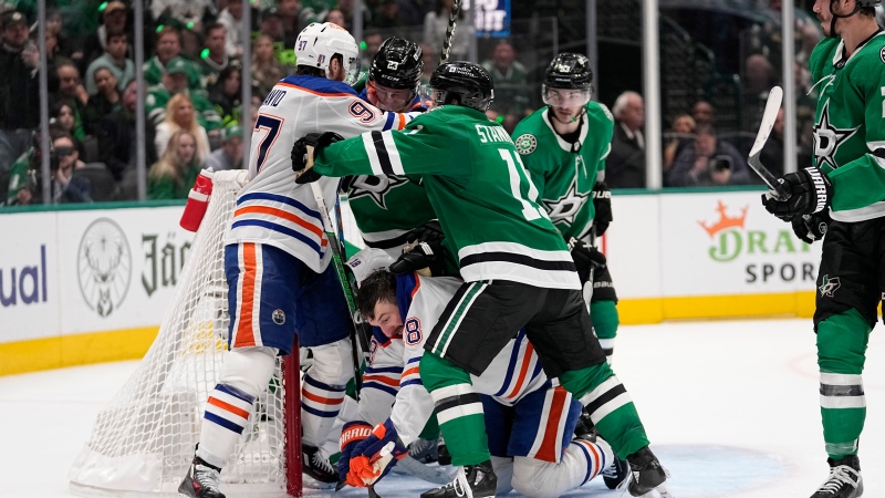 Edmonton Oilers left wing Zach Hyman, bottom center, loses his helmet on a shot as Oilers' Connor McDavid, top left, and Dallas Stars' Logan Stankoven (11) scuffle at the net during the second period in Game 2 of the Western Conference finals in the NHL hockey Stanley Cup playoffs Saturday, May 25, 2024, in Dallas. (AP Photo/Tony Gutierrez)