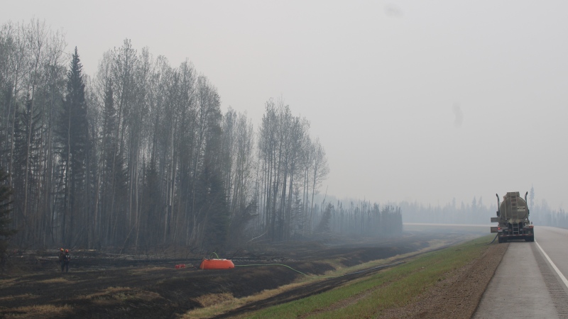 Firefighters working the Parker Lake wildfire, designated G90267 by the B.C. Wildfire Service, are seen in a staging area along Highway 97 looking south with a water bladder and fire hose set up among charred grassland in a May 15, 2024, handout photo. THE CANADIAN PRESS/BC Wildfire Service