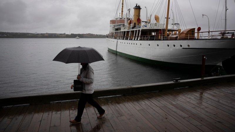 A pedestrian shields themselves with an umbrella while walking along the Halifax waterfront as rain falls ahead in Halifax on Sept. 23, 2022. THE CANADIAN PRESS/Darren Calabrese